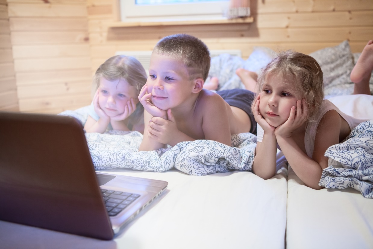 children looking-at computer monitor while laying in bed