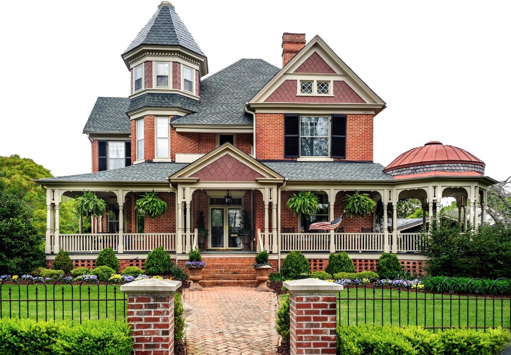 large red brick with white trim victorian house with wrap around veranda